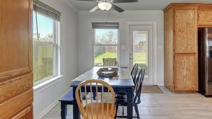 A kitchen with a dining table, chairs, a ceiling fan, and a view of the backyard through the windows. - A Wave From It All 3 Bedroom Home by RedAwning (Rockport)