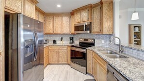 A modern kitchen with wooden cabinets, stainless steel appliances, a granite countertop, and a tiled backsplash. - A Wave From It All 3 Bedroom Home by RedAwning (Rockport)