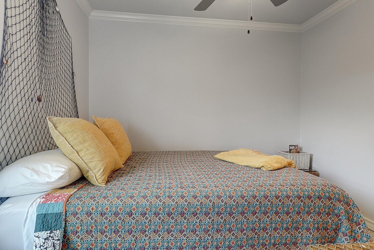 Un letto singolo con copriletto decorato, due cuscini, un comodino con lampada e una zanzariera appesa.