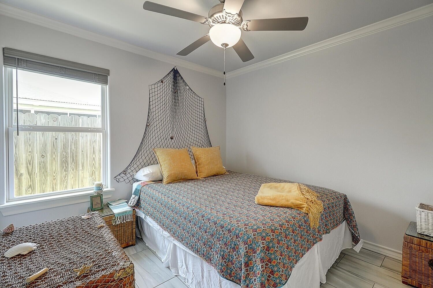 A bedroom with a bed, a ceiling fan, a window with a view, and a small table with a basket.