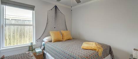 A bedroom with a bed, a ceiling fan, a window with a view, and a small table with a basket.