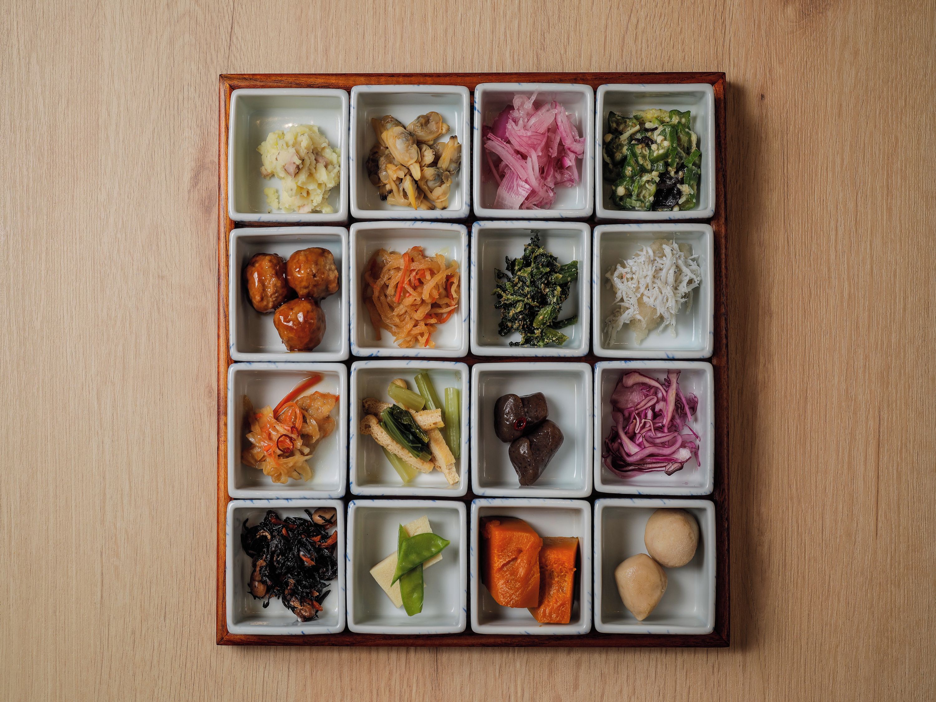 A wooden table with a grid of square dishes containing various food items.
