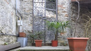 Uma escadaria de pedra leva a uma porta com portão de ferro forjado, cercada por plantas em vasos.
