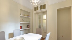 Uma sala de jantar com uma mesa branca, cadeiras e prateleiras com utensílios de cozinha.