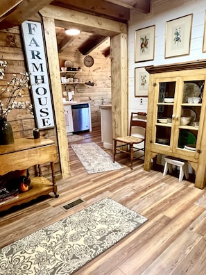Um interior rústico com piso de madeira, um letreiro 'Farmhouse', um armário de madeira e uma área de refeições.