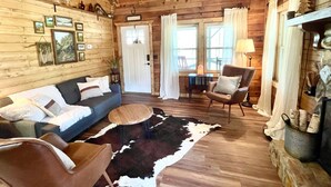 L’intérieur chaleureux d’un chalet, avec un revêtement mural en bois, un canapé, un fauteuil, un tapis et une cheminée.