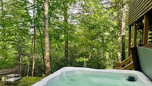 Un bain à remous situé dans un espace boisé, avec une terrasse en bois et du mobilier d’extérieur.