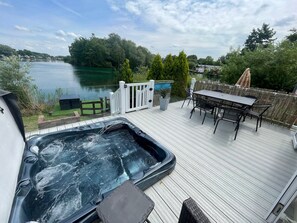 A deck with a hot tub, outdoor furniture, and a view of a lake.