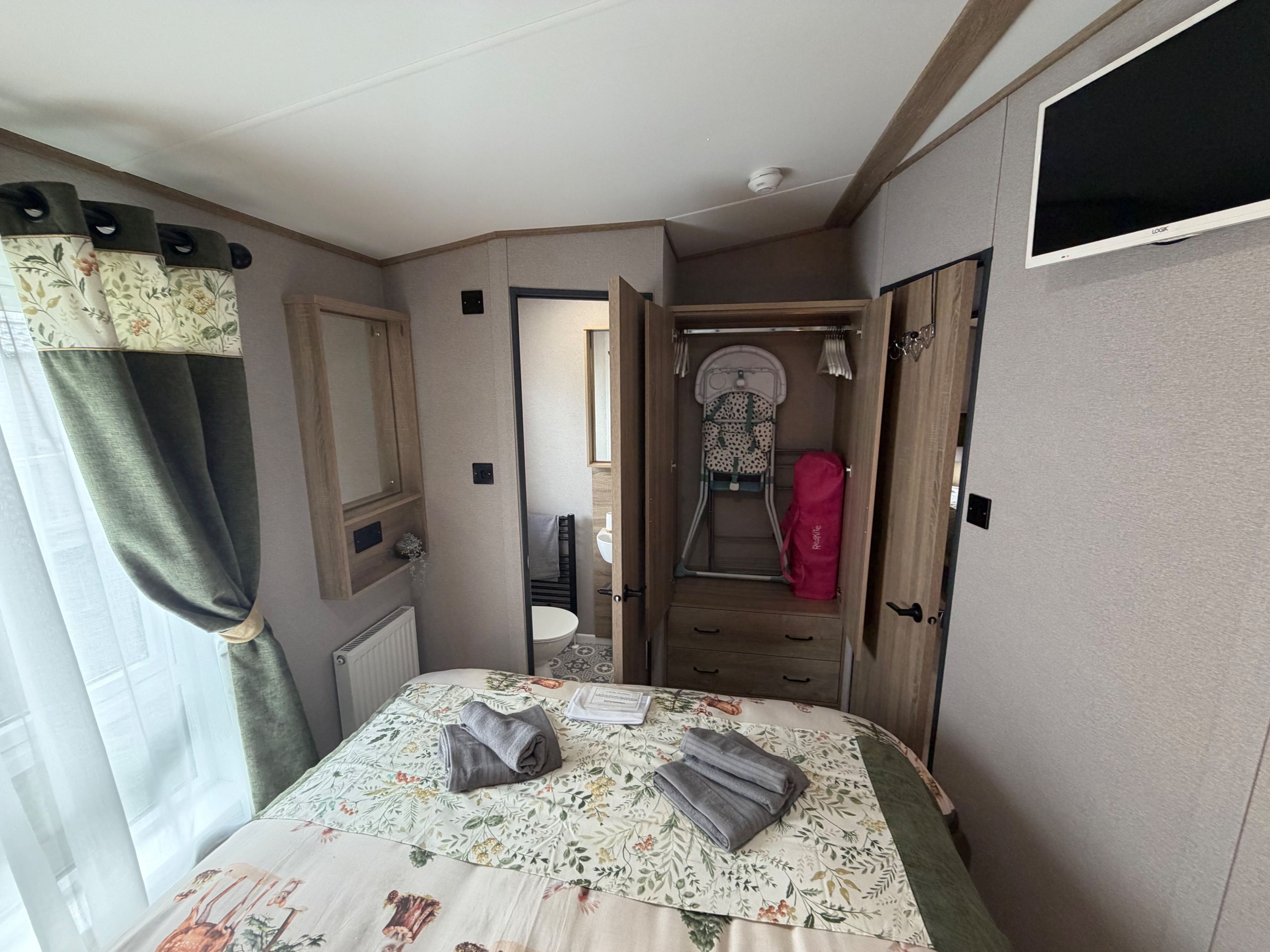 A compact bedroom with a bed, a wardrobe, a mirror, and a bathroom visible through an open door.