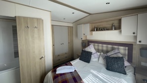 Un dormitorio con cama, armario, cómoda y estante con objetos decorativos.