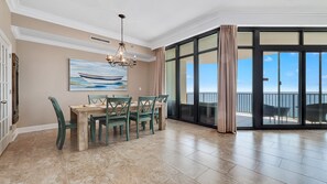 Un coin repas avec une table et des chaises, un tableau représentant un bateau et une vue sur l’océan par de grandes portes coulissantes.