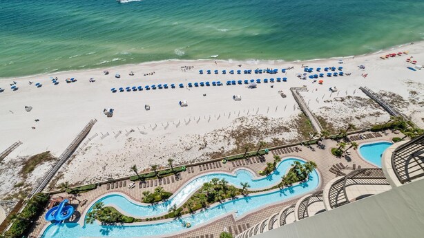 Vista aerea di un resort sulla spiaggia con piscina, ombrelloni e lettini.