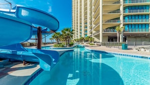 Una piscina con uno scivolo acquatico, palme e un edificio a più piani sullo sfondo.