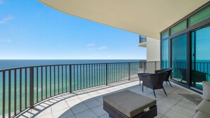 Un balcone con vista sull'oceano, un tavolo con sedie e una panca imbottita.