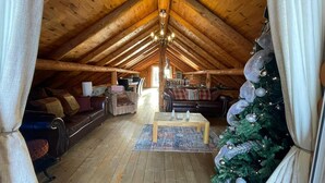 A cozy attic room with wooden beams, a Christmas tree, and a fireplace.