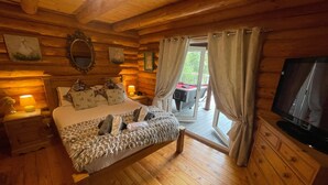 A wooden cabin bedroom with a bed, a television, and a view of an outdoor deck.