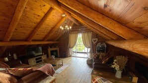 A cozy attic room with wooden beams, a fireplace, a television, and comfortable seating.