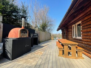Una terraza de madera con un horno de pizza y una mesa de picnic.