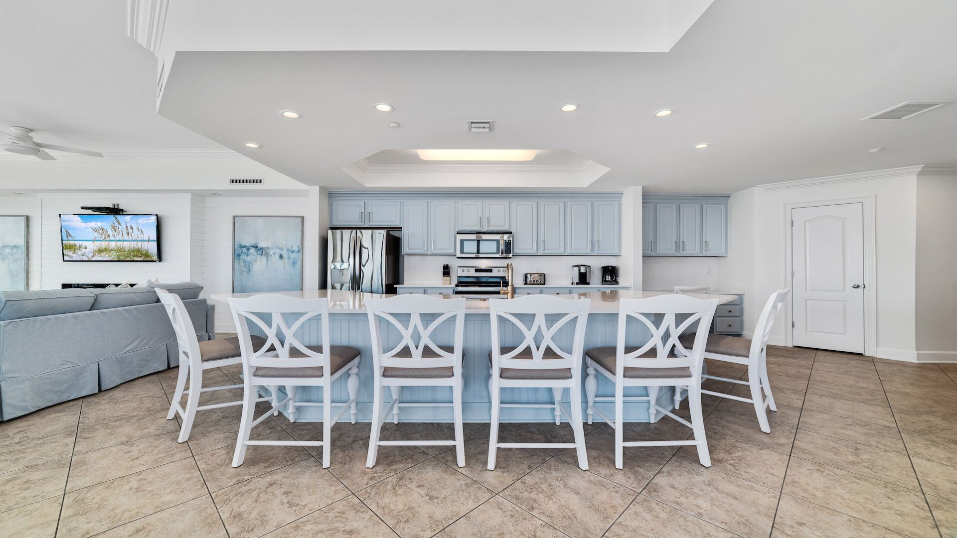 A modern kitchen with light blue cabinets, a central island with white chairs, and a dining table.