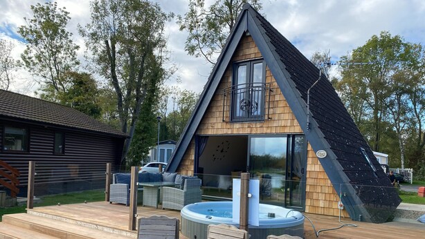 A wooden cabin with a sloped roof, a hot tub, and outdoor seating.