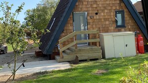 A small wooden cabin with a sloped roof, a wooden deck, and a fire extinguisher nearby.