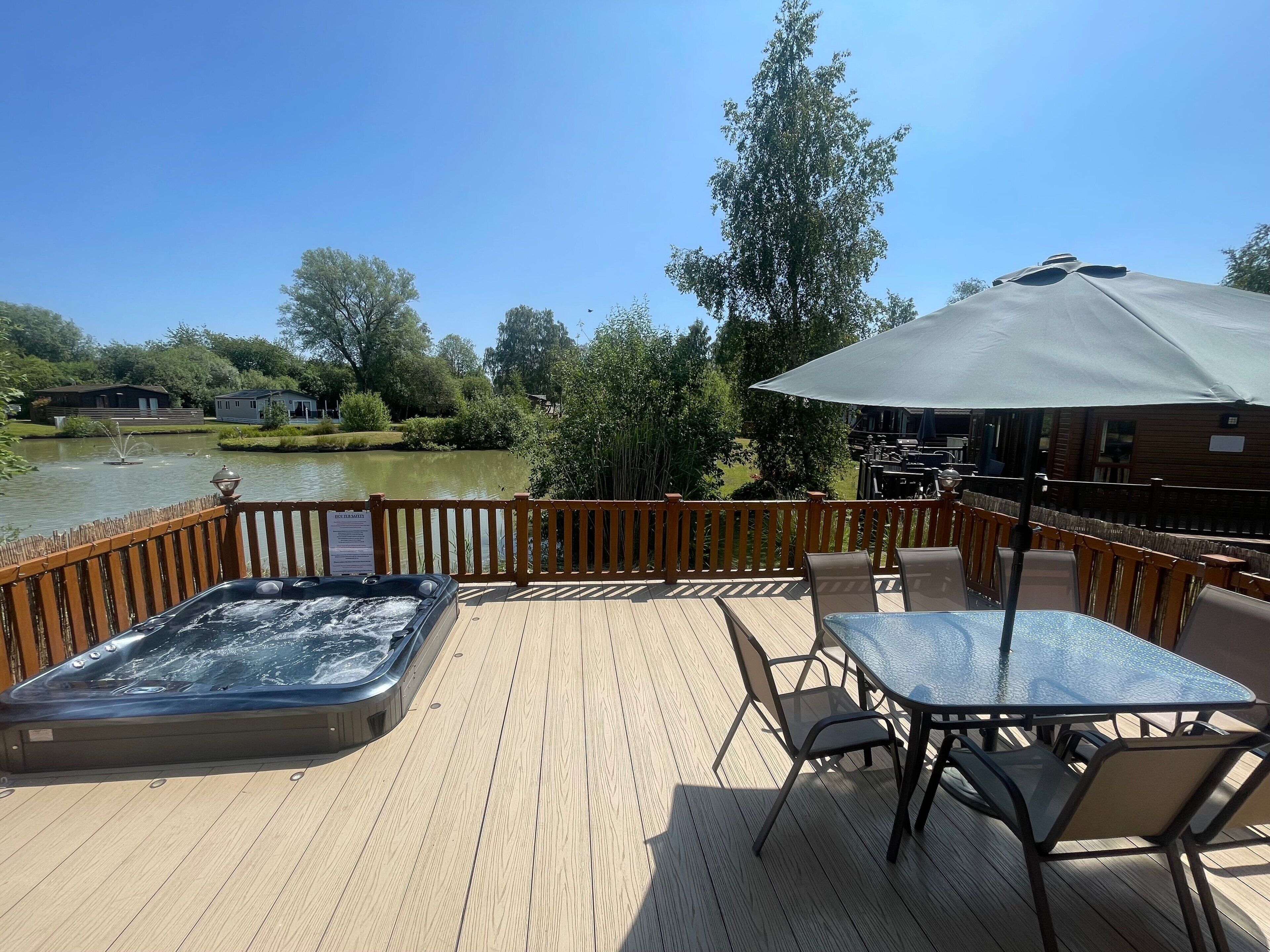 Een houten terras met een jacuzzi, zitplaatsen buiten en uitzicht op een meer.