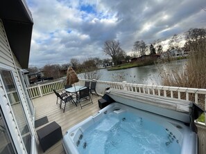Relax on the deck overlooking the serene water, where a hot tub and comfortable seating await.