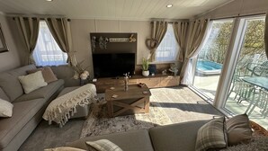 A living room with a sofa, a coffee table, a TV, and a view of a swimming pool. - Luxury lakeside lodge with sunken hot tub prime location on bull rush lake @tattershall lakes (Tattershall)