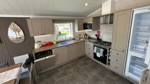 A modern kitchen with a built-in stove, microwave, and refrigerator, a window with a view, and a dishwasher. - Luxury lakeside lodge with sunken hot tub prime location on bull rush lake @tattershall lakes (Tattershall)