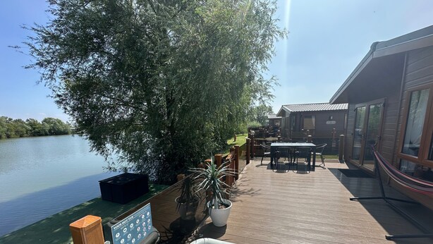 Eine Holzterrasse mit Whirlpool, Gartenmöbeln und Blick auf einen ruhigen See.