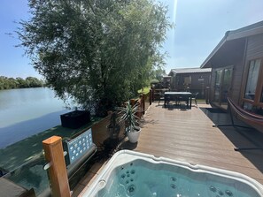 A wooden deck with a hot tub, outdoor furniture, and a view of a calm lake.