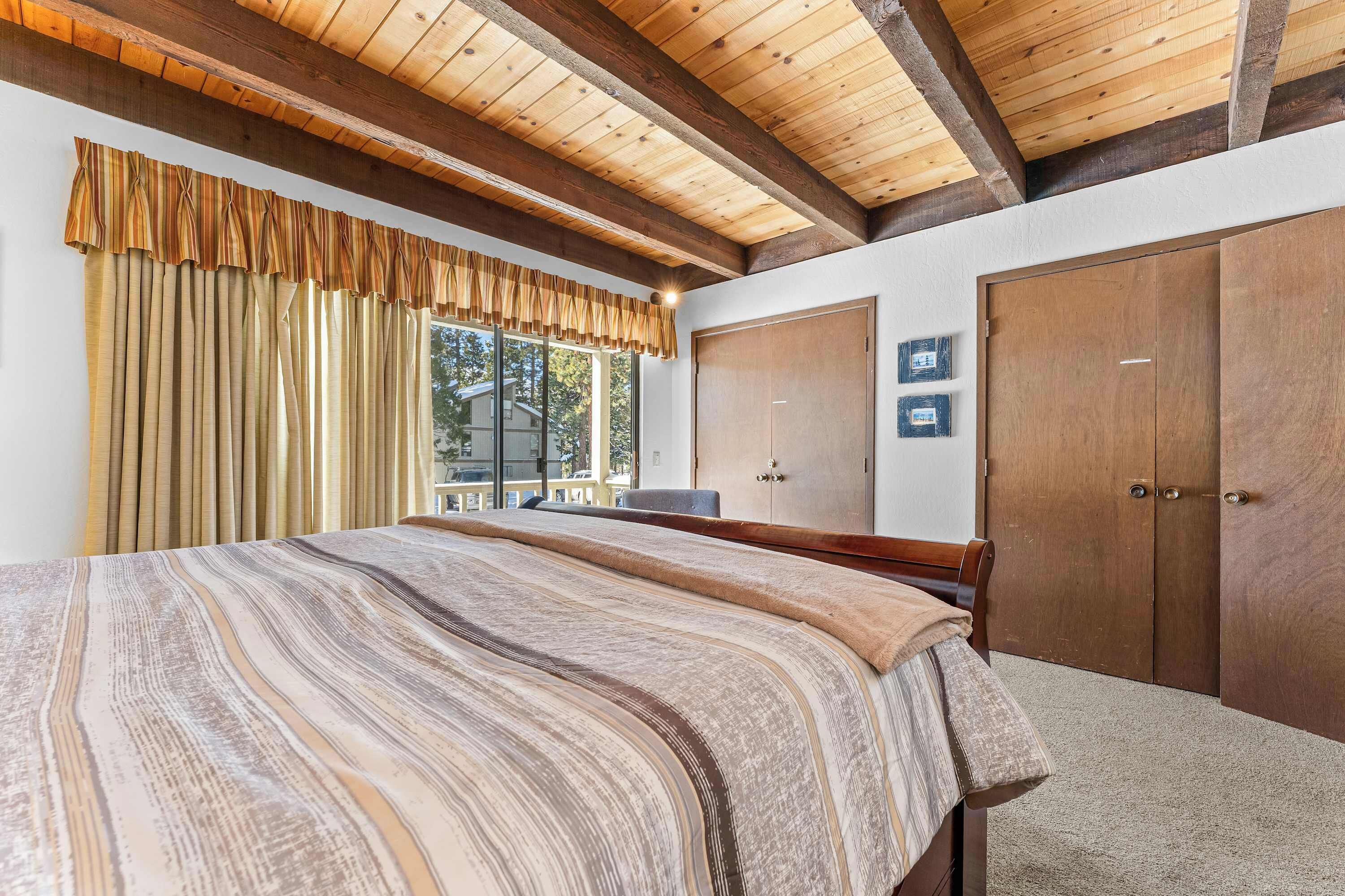 Een slaapkamer met een groot bed, houten balken in het plafond, een kledingkast en een raam met gordijnen.