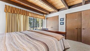 Een slaapkamer met een groot bed, houten balken in het plafond, een kledingkast en een raam met gordijnen.
