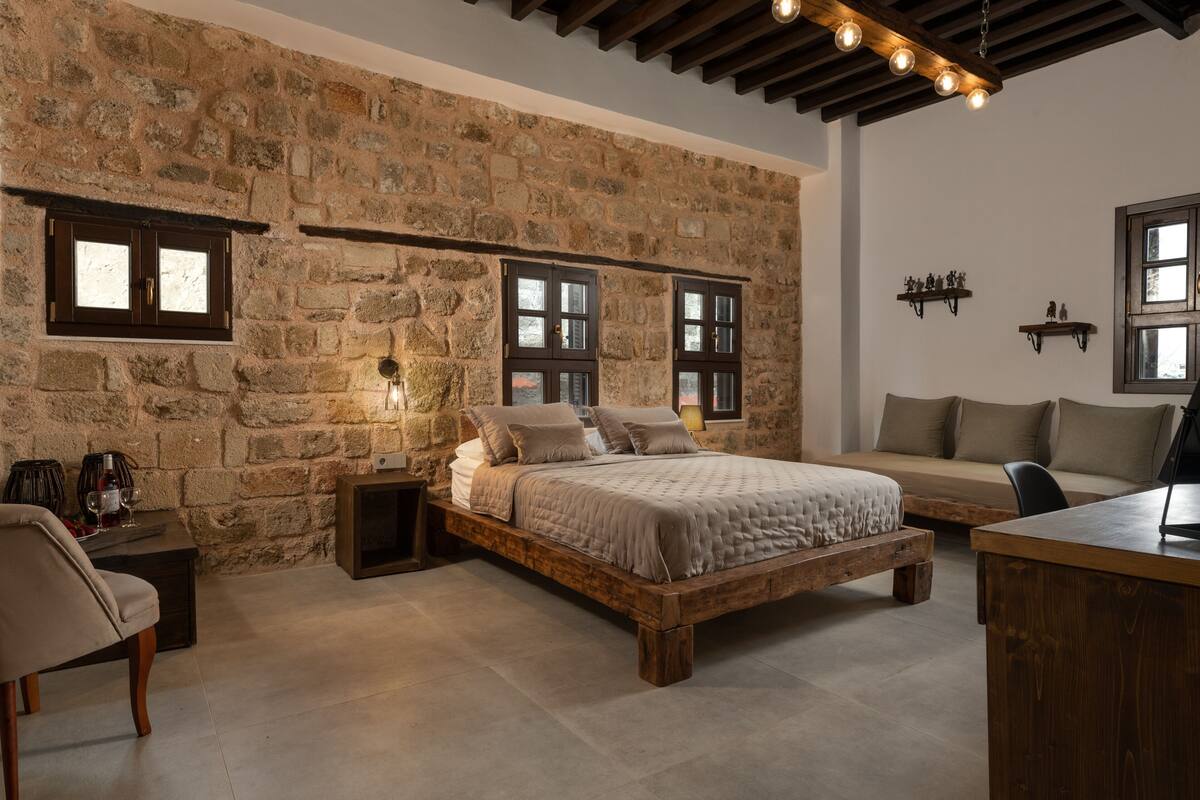 Un dormitorio con pared de piedra, cama de madera, sofá y escritorio.