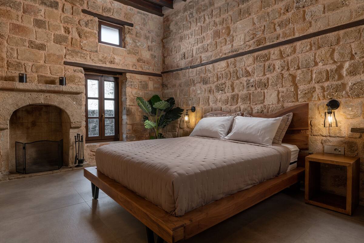 Un dormitorio con pared de piedra, chimenea, cama y mesita de noche.