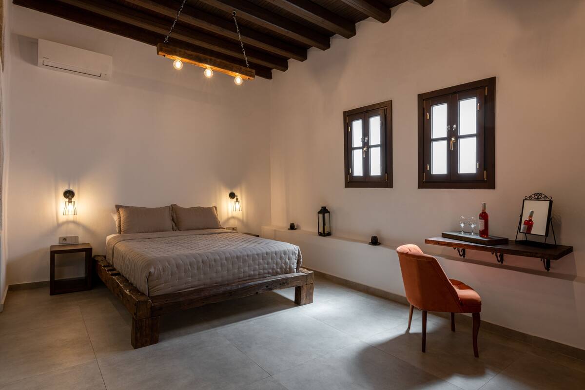 Un dormitorio con una cama de madera, una mesita de noche, una silla y dos ventanas.