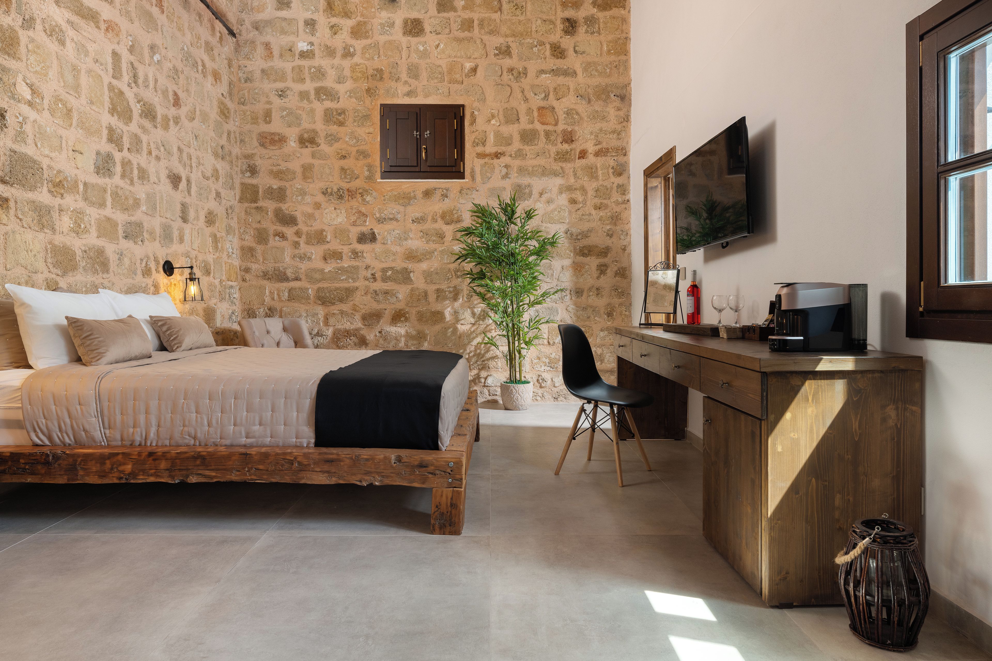 Un dormitorio con pared de piedra, una cama, un escritorio, una silla, una planta en maceta, un televisor y una cafetera.