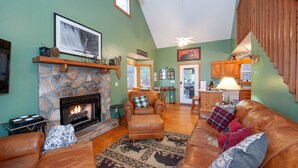A cozy living room with a stone fireplace, leather furniture, and a staircase leading to another level.