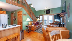 A spacious living area with a wooden staircase, a kitchen with a refrigerator, and a dining area with a bench.