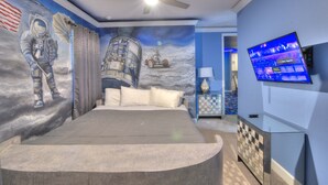 Quarto com uma cama grande, ventilador de teto, televisão e um mural de astronautas e uma nave espacial.
