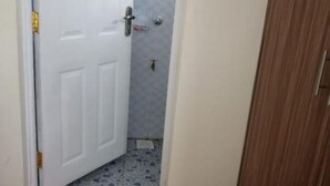 Een kamer met een witte deur, een klein betegeld douchegedeelte en een paar rode slippers op een mat.