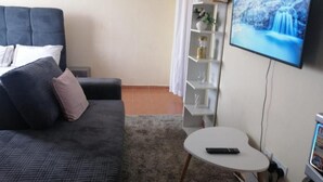 Een slaapkamer met een bed, een klein wit tafeltje, een televisie aan de muur en een plank met decoratieve objecten.
