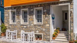 A two-story building with orange walls and white trim, stone facade, and a set of outdoor tables and chairs. - Meraki Bozcaada (Bozcaada)