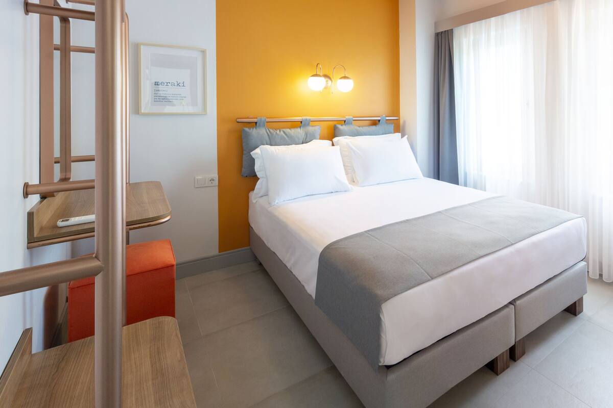 Quarto de hotel com cama, escrivaninha, cadeira e quadro na parede.
