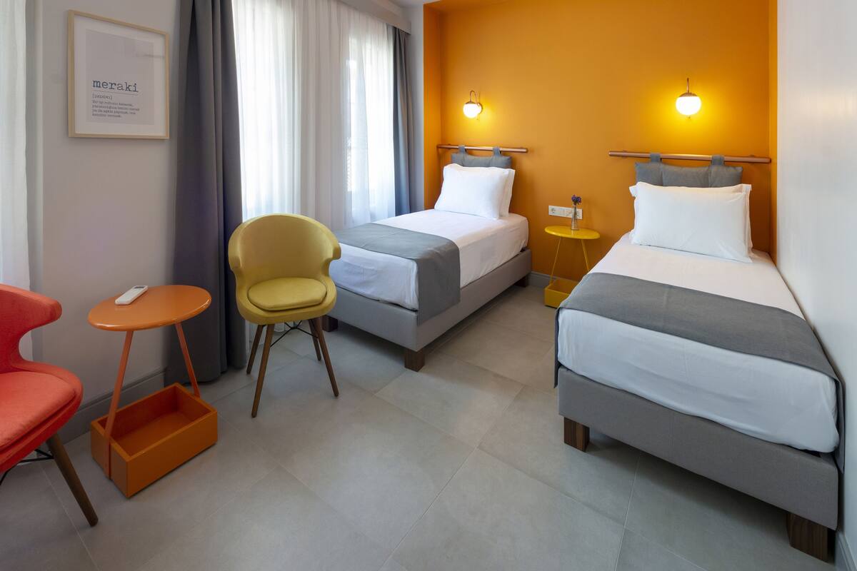 Quarto de hotel com duas camas, uma mesa pequena, uma cadeira e um quadro na parede.