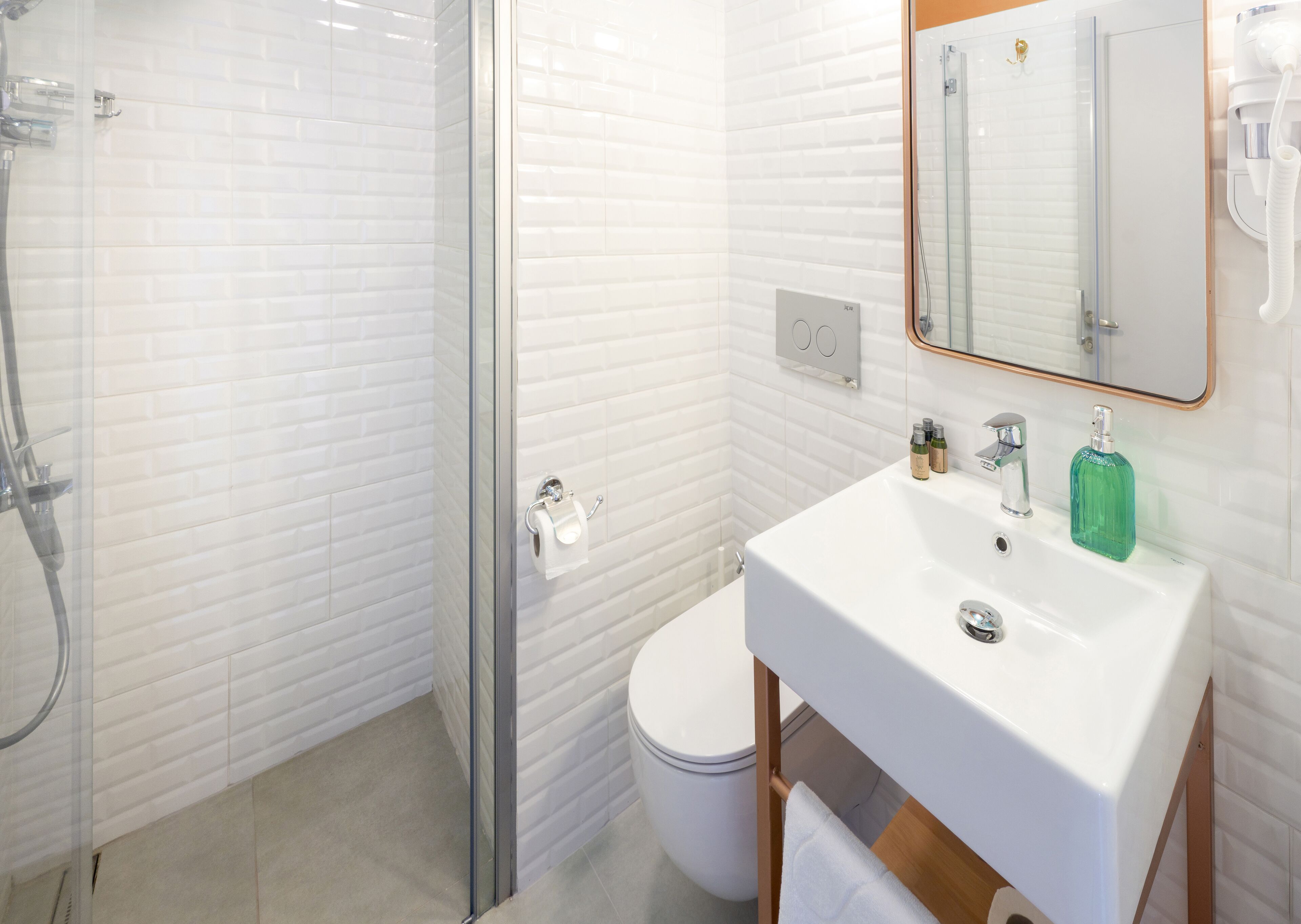 A modern bathroom with a glass shower enclosure, a white toilet, and a sink with a mirror above it.