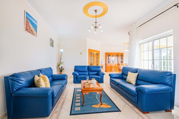 A living room with blue leather sofas, a wooden coffee table, and a chandelier.