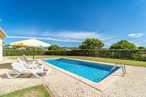 A rectangular swimming pool with a tiled deck, surrounded by a hedge and a clear blue sky.