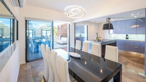 A modern kitchen with a central island, a dining area with a glass table, and a view of the outdoors.