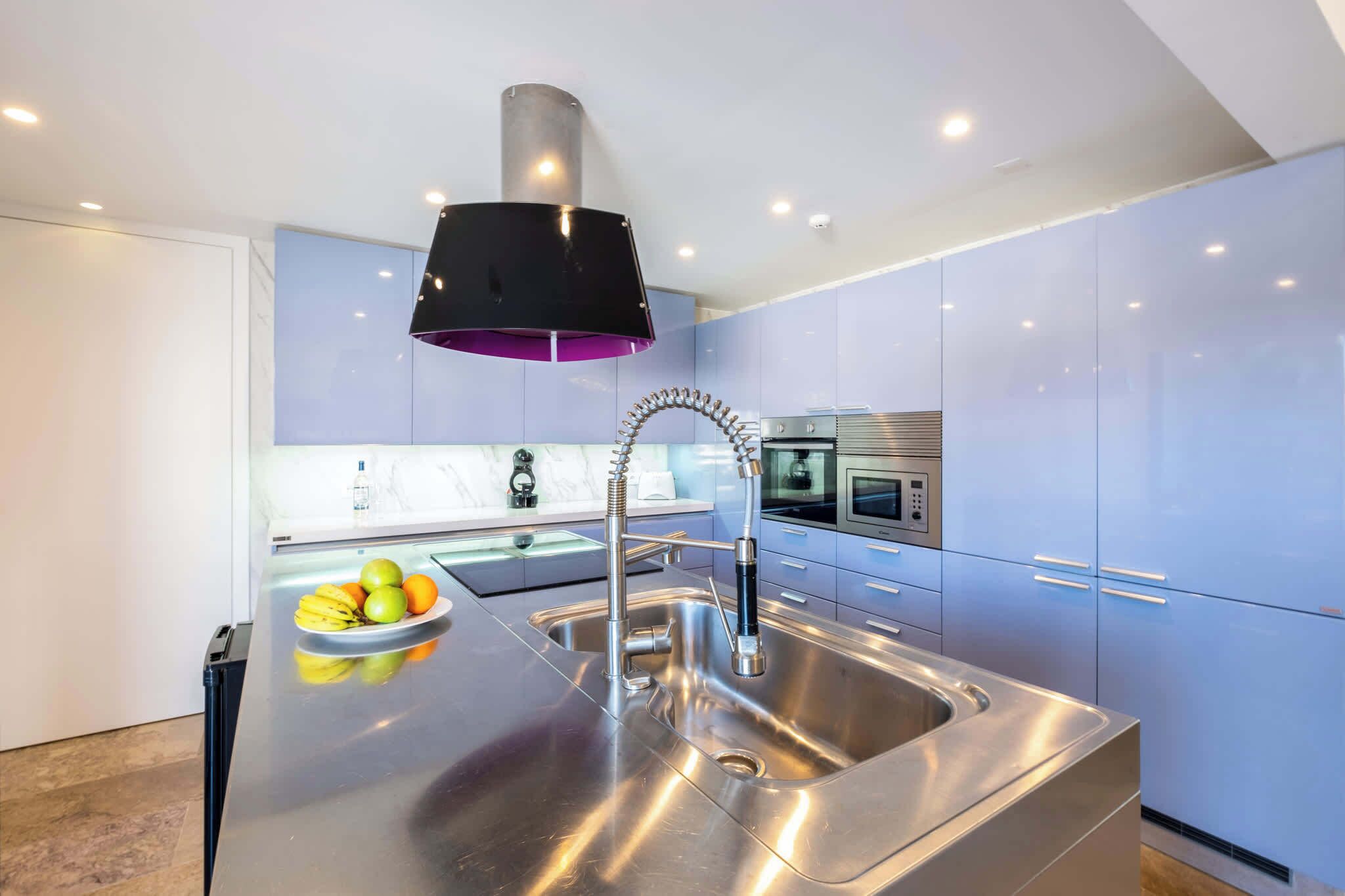 A modern kitchen with stainless steel appliances, a central island with a sink, and a black pendant light.
